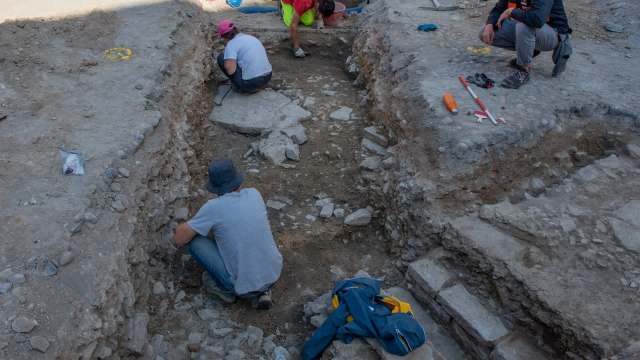 Several people are working in a rocky excavation site, uncovering layers of soil and stones.