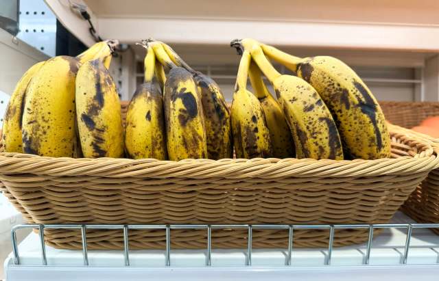 A woven basket filled with ripe, spotted bananas on a store shelf.