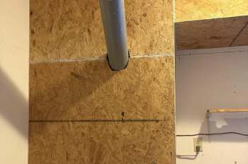 A vertical metal pipe passes through an opening in an oriented strand board wall.