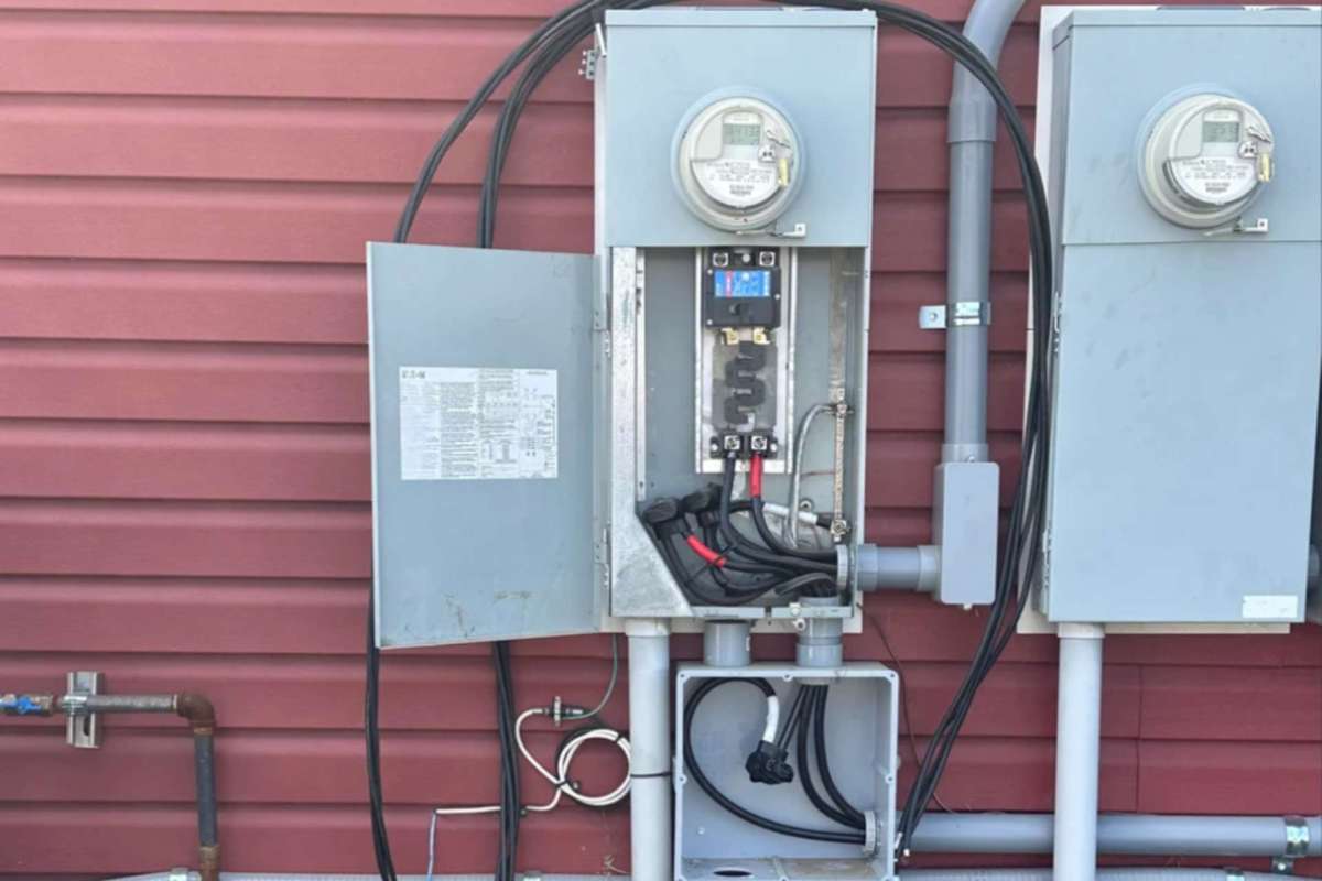 An electrical panel with meters and cables mounted on a red exterior wall.