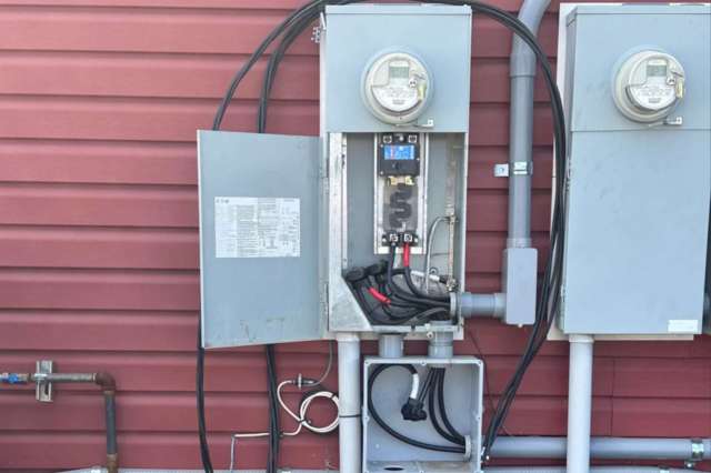 An electrical panel with meters and cables mounted on a red exterior wall.