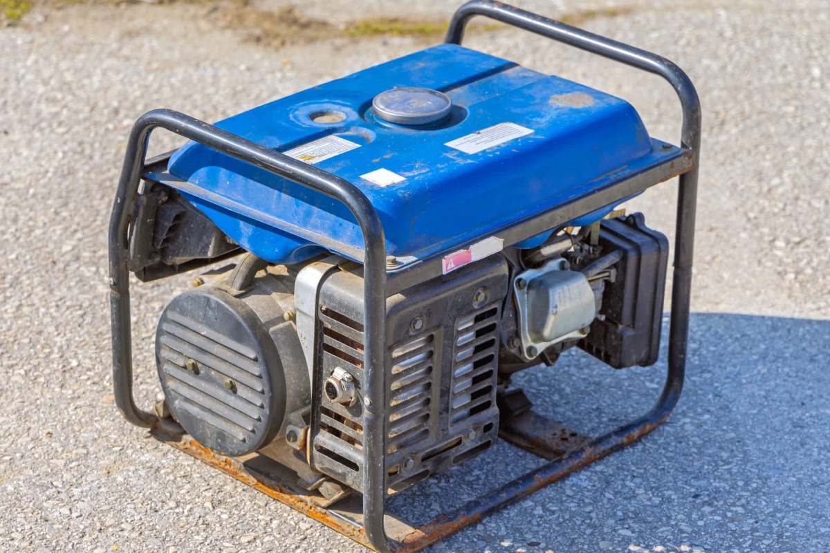 A portable generator with a blue top and metal frame on a gravel surface.