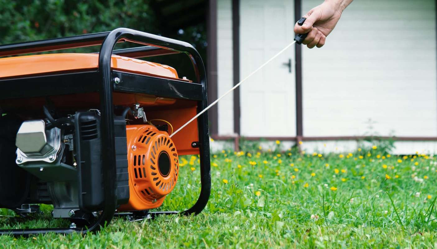 A person starts a portable generator on a lawn.