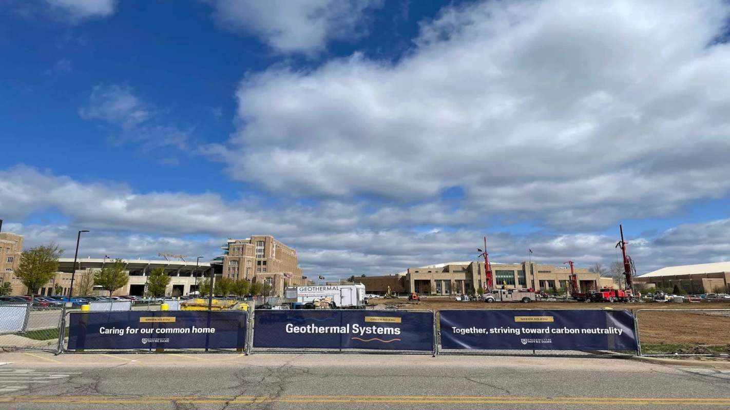 Construction site with a "Geothermal Systems" banner and machinery, under a partly cloudy sky.