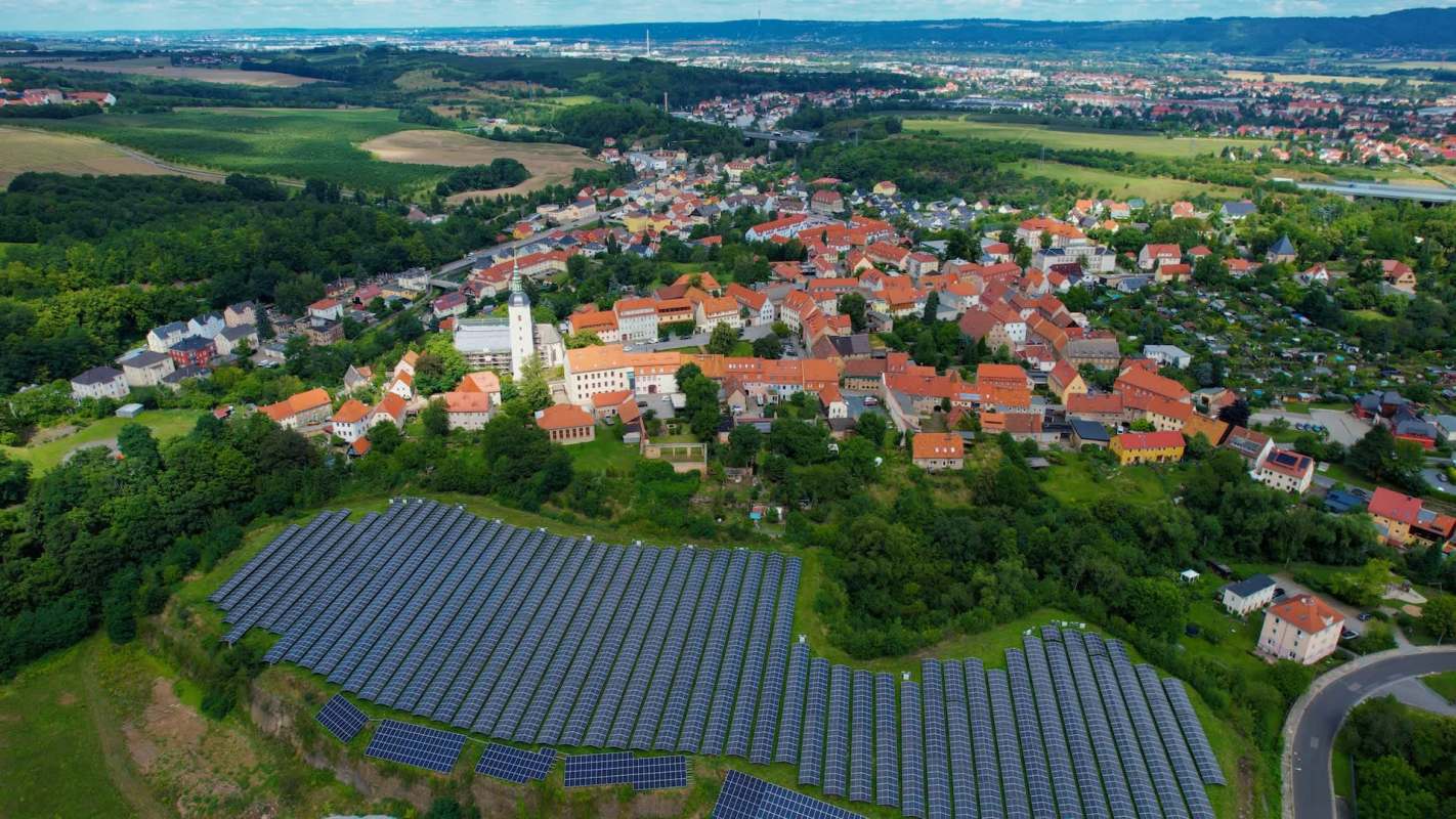 A town with red-roofed buildings near a large solar panel installation and green fields.