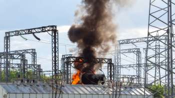 A power substation with a fire and thick black smoke rising from the equipment.