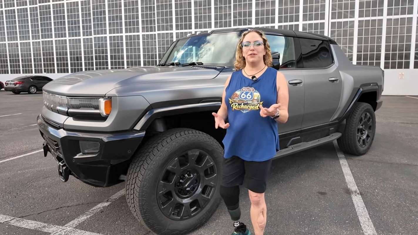 A woman stands next to a gray SUV in a parking lot.