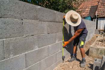 A person measures a concrete block wall with a tape measure in a construction area.