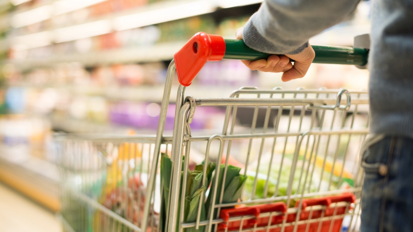 A person pushing a shopping cart filled with groceries in a supermarket aisle.