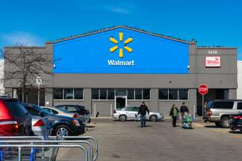 A Walmart store exterior with customers walking and parked cars in the lot.