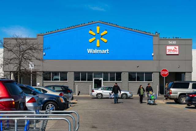 A Walmart store exterior with customers walking and parked cars in the lot.
