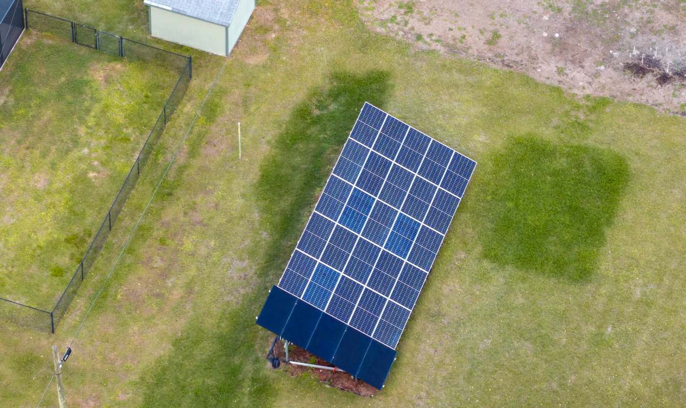 A solar panel array on a grassy area near a small building and a fenced-off section.