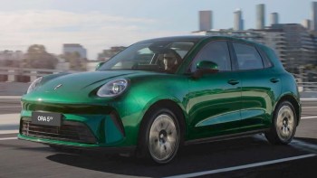 A green GWM Ora 5 electric car driving on a city road.