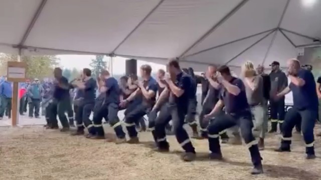 A group of firefighters perform a haka dance under a tent.