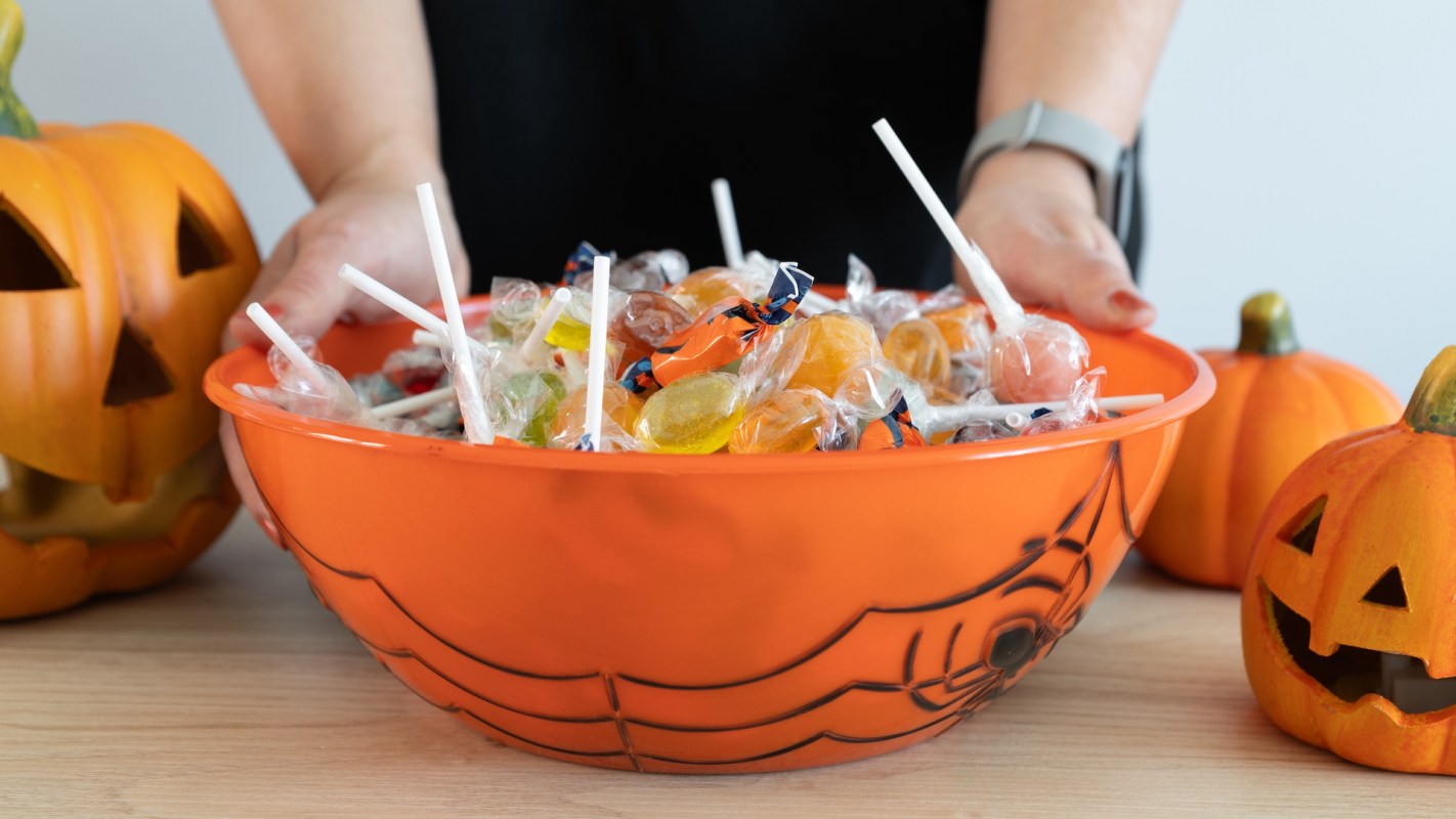 A bowl of assorted candies surrounded by carved Halloween pumpkins.