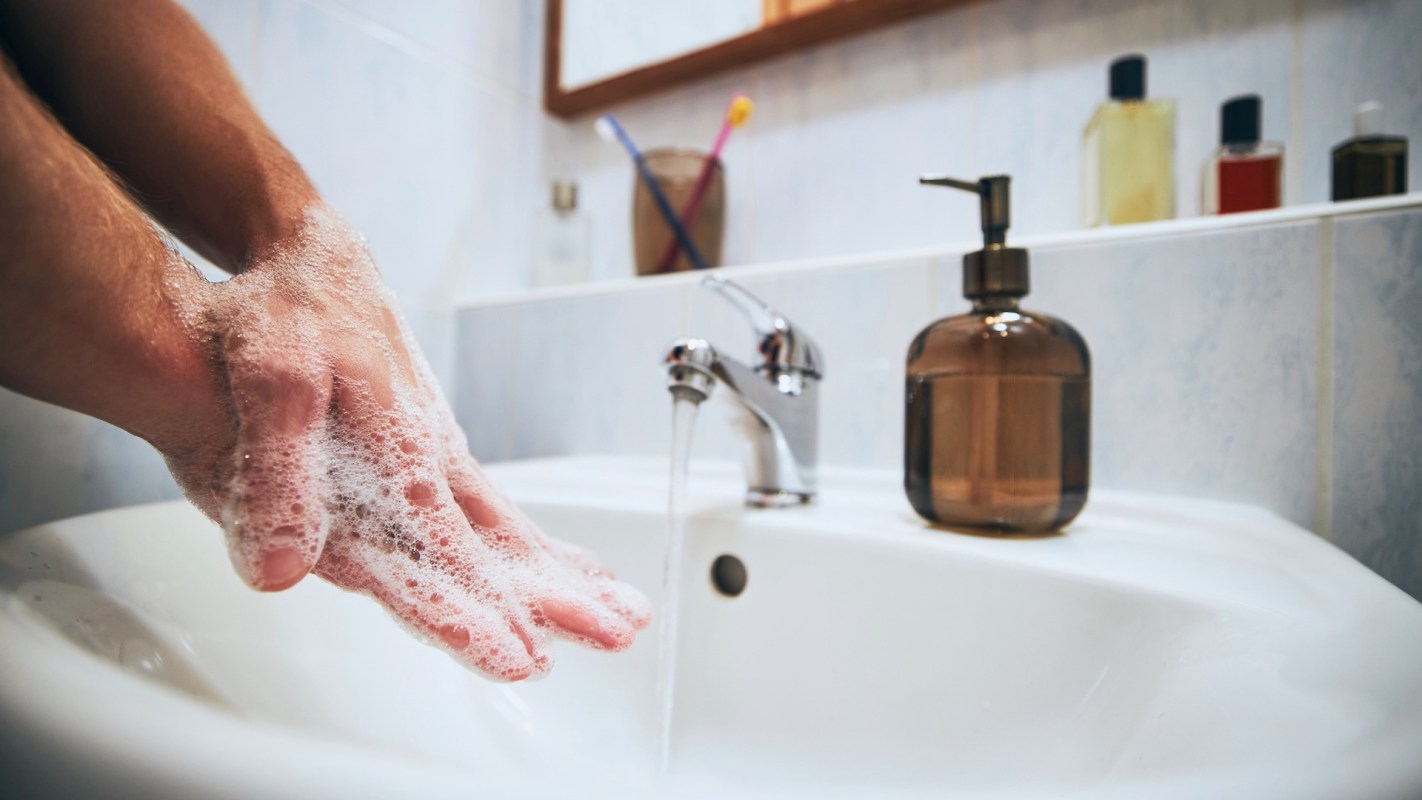 A person washes their hands with soap at a bathroom sink.