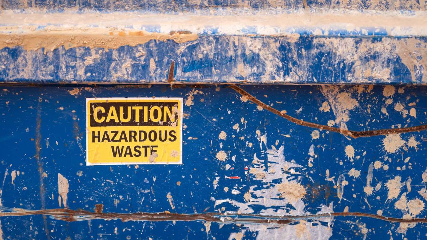 A blue dumpster with a caution sign indicating hazardous waste.