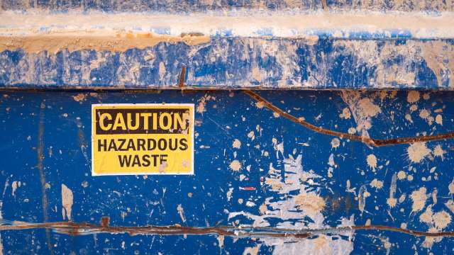 A blue dumpster with a caution sign indicating hazardous waste.