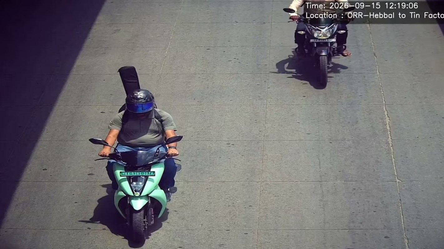 Two riders on motorcycles are seen on a road, one carrying a guitar case.