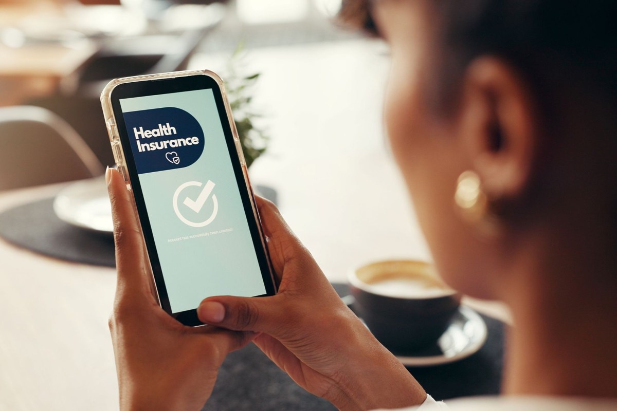 A woman holds a phone with a screen that reads health insurance with a check mark