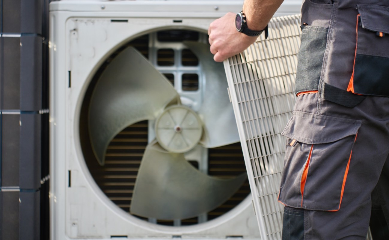 A technician holds a filter while servicing an outdoor air conditioning unit.