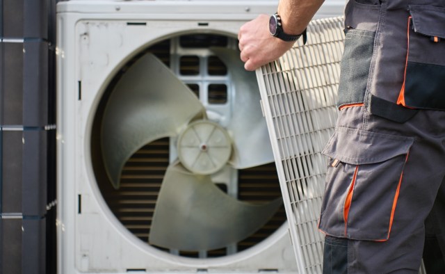 A technician holds a filter while servicing an outdoor air conditioning unit.