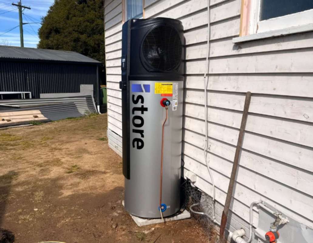 A large cylindrical storage unit with a fan attached, positioned outside a wooden building.
