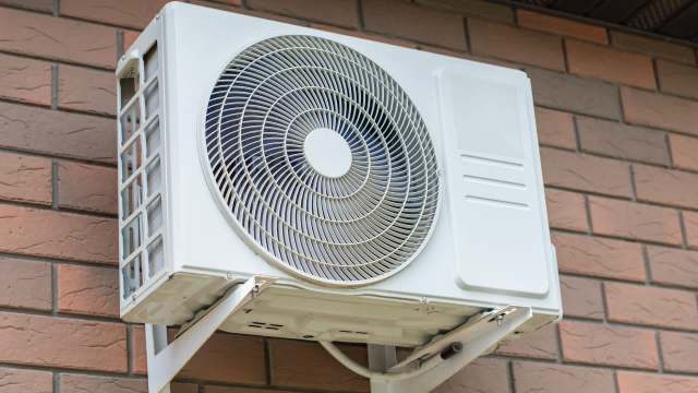 A heat pump unit mounted on a brick wall.