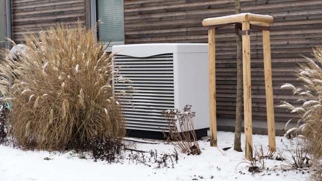 An outdoor area with snow, a large HVAC unit, ornamental grasses, and a wooden tree support structure.
