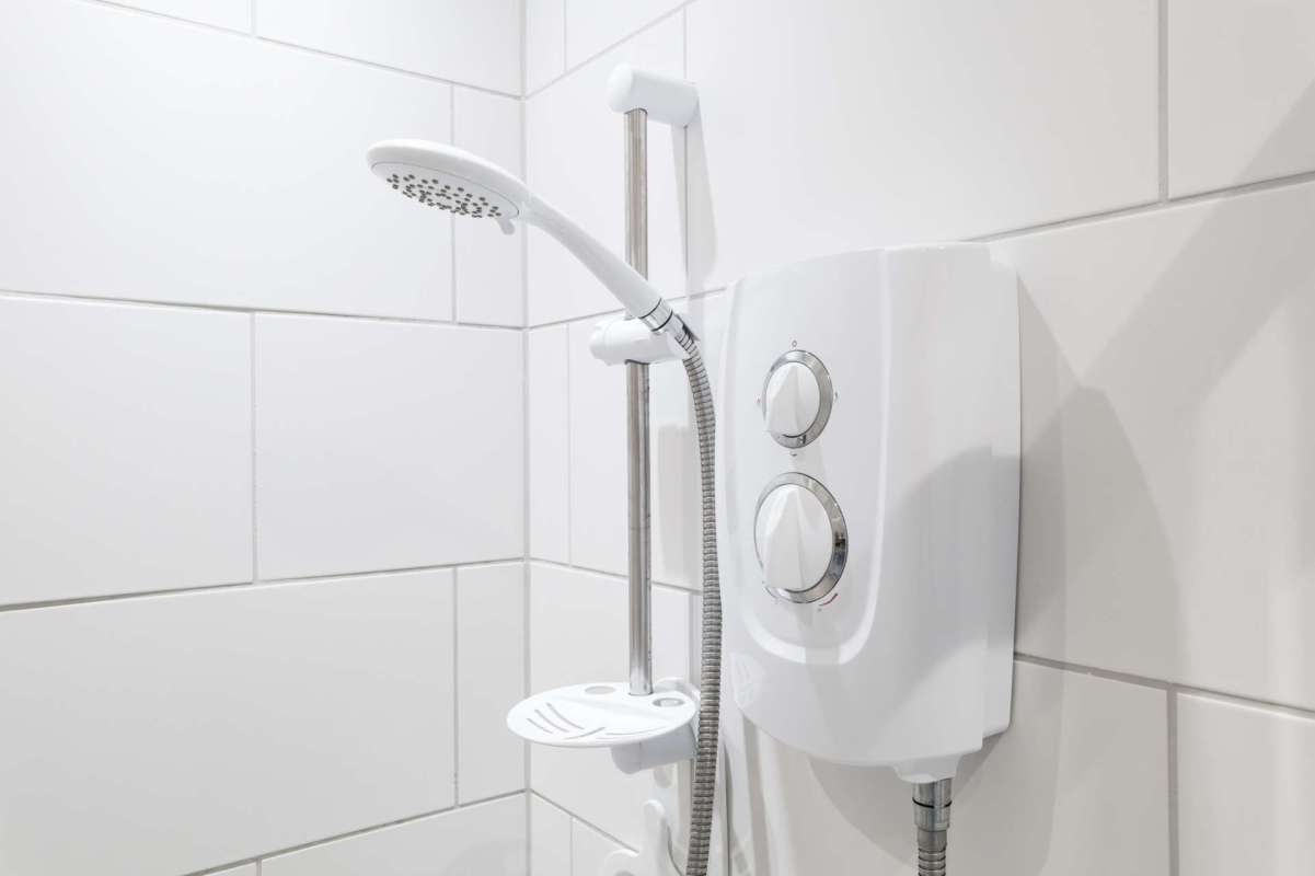 A showerhead and control unit mounted on white tiled bathroom wall.