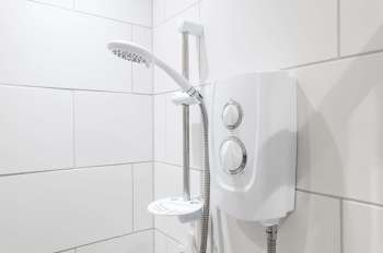 A showerhead and control unit mounted on white tiled bathroom wall.