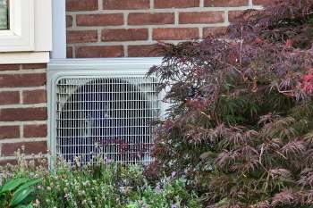 A heat pump along a brick wall.