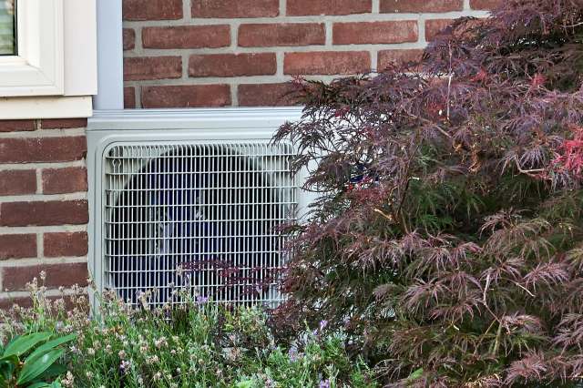 A heat pump along a brick wall.