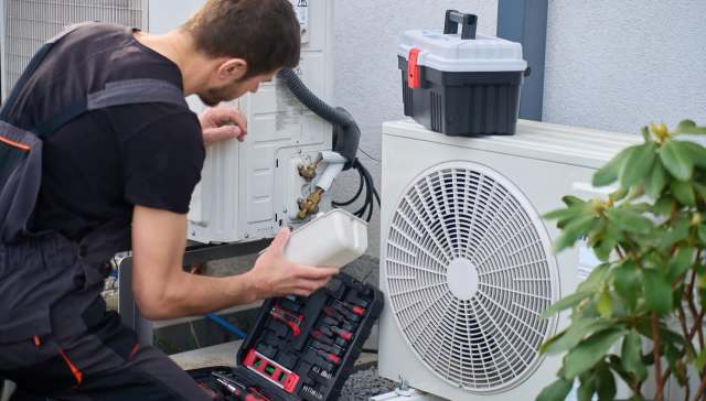 A technician works on an outdoor air conditioning unit with tools nearby.
