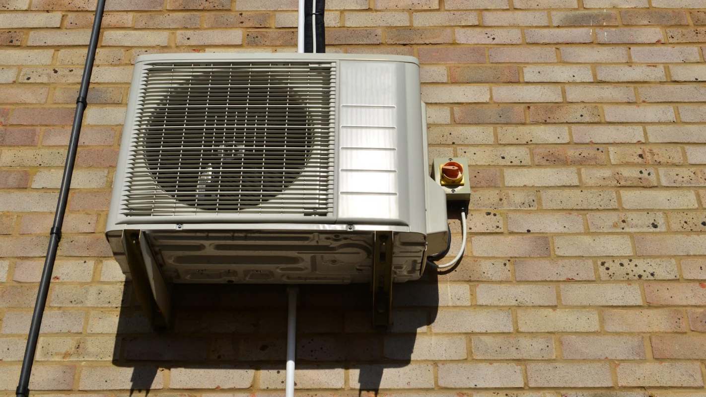 An air conditioning unit mounted on a brick wall with visible wiring and a power switch.