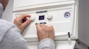 A person adjusts the temperature settings on a heating control panel.