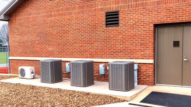 Three air conditioning units are mounted against a red brick wall next to a door.