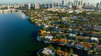 An aerial view of a waterfront neighborhood with houses, canals, and tall buildings in the background.