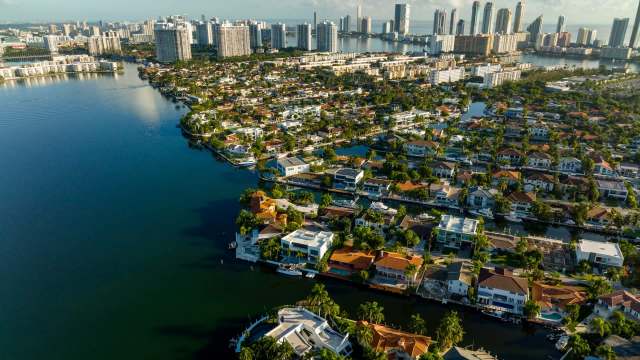 An aerial view of a waterfront neighborhood with houses, canals, and tall buildings in the background.