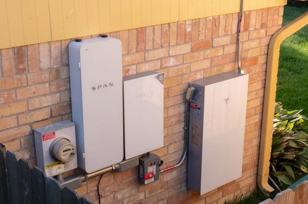 Electrical equipment mounted on a brick wall, including a meter, batteries, and a power management system.