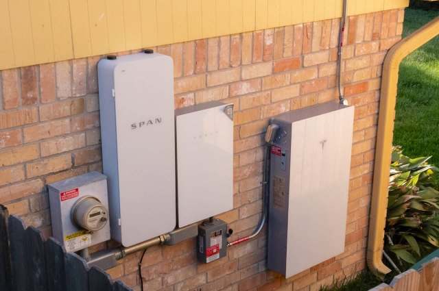 Electrical equipment mounted on a brick wall, including a meter, batteries, and a power management system.