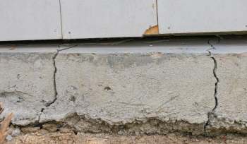 A cracked concrete foundation with exposed soil underneath.
