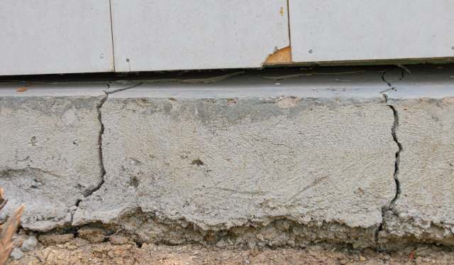 A cracked concrete foundation with exposed soil underneath.