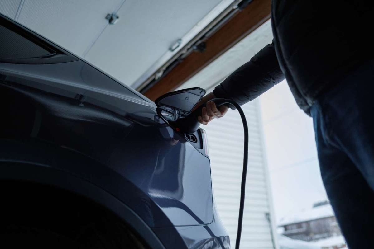 A person plugs an electric vehicle charging cable into a car in a garage.