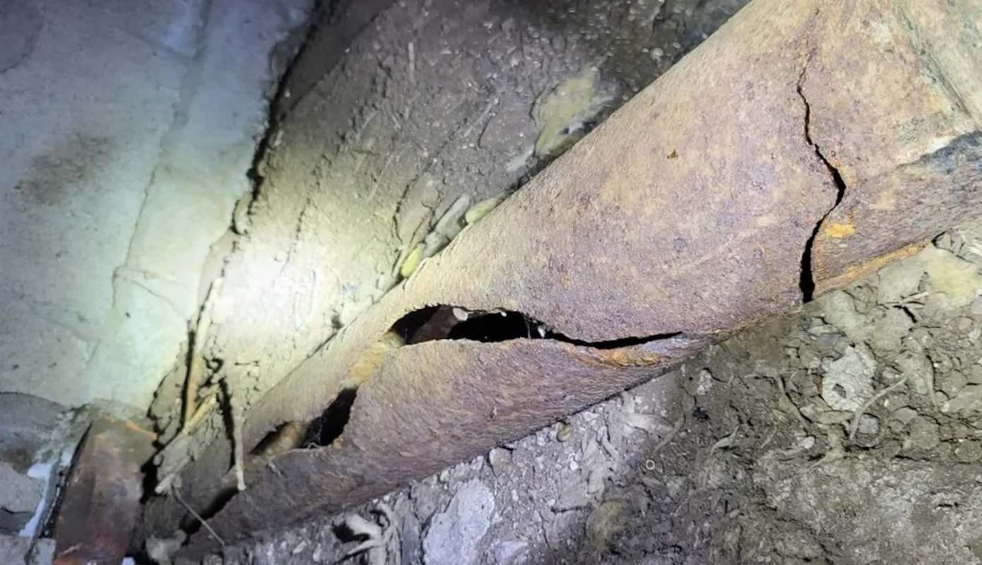 A cracked metal pipe sits in a dusty, dark environment.