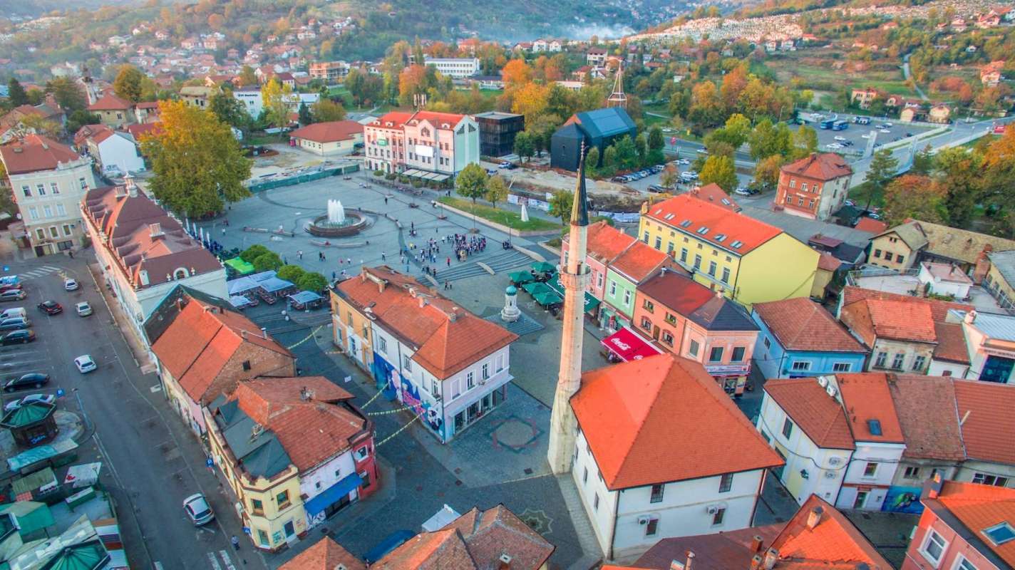 Aerial view of a town square with a fountain, mosque, and colorful buildings.