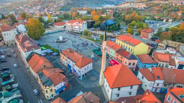 Aerial view of a town square with a fountain, mosque, and colorful buildings.