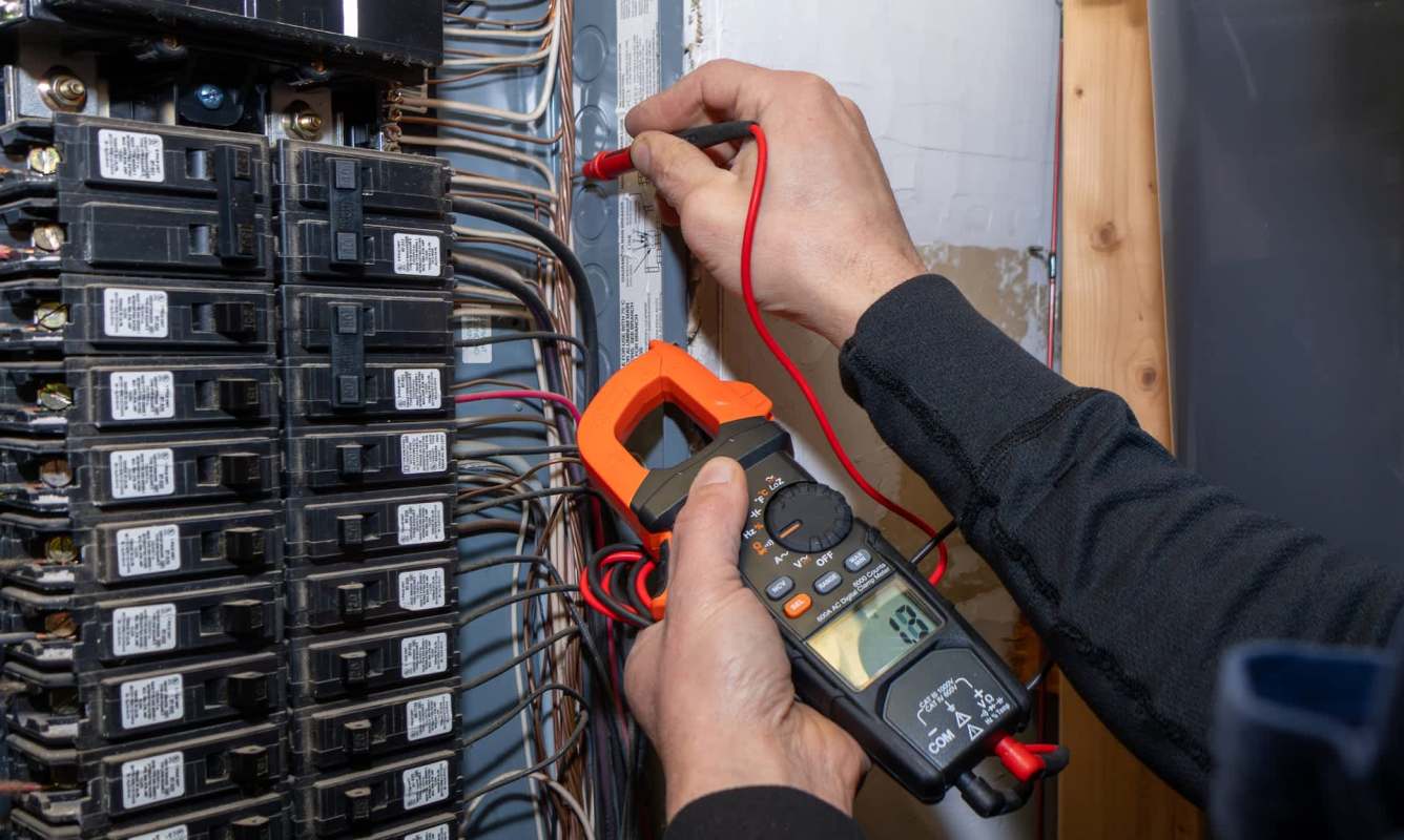 A person uses a multimeter to test electrical connections in a breaker box.