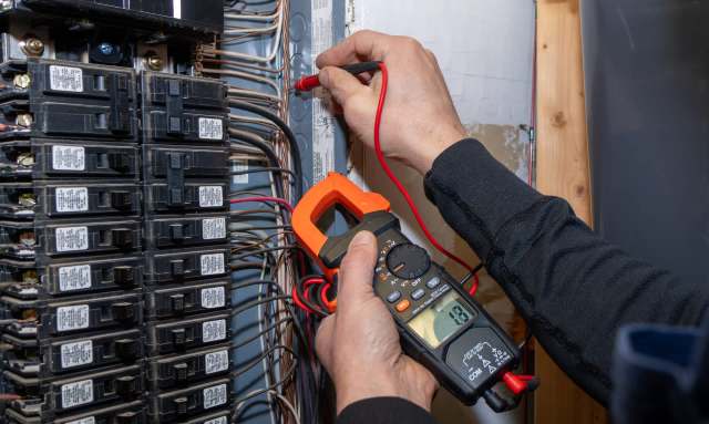 A person uses a multimeter to test electrical connections in a breaker box.