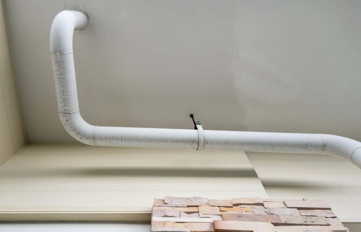 A white pipe runs along a ceiling near a stone wall.